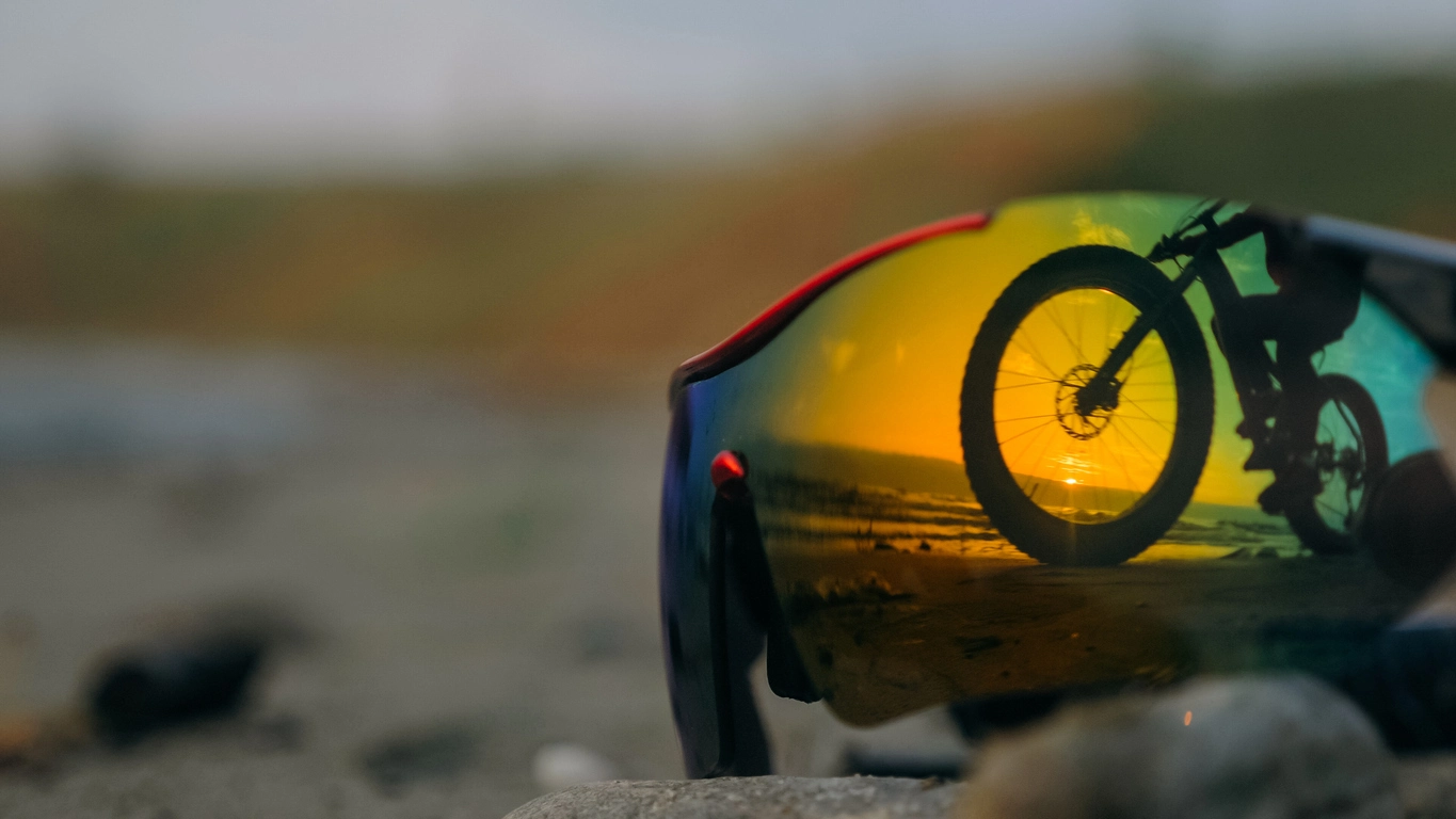 Sport-Sonnenbrille mit Spiegelglas reflektiert Mountainbike-Fahrer bei Sonnenuntergang – optimal für Sport, Outdoor &amp; sicheres Autofahren.