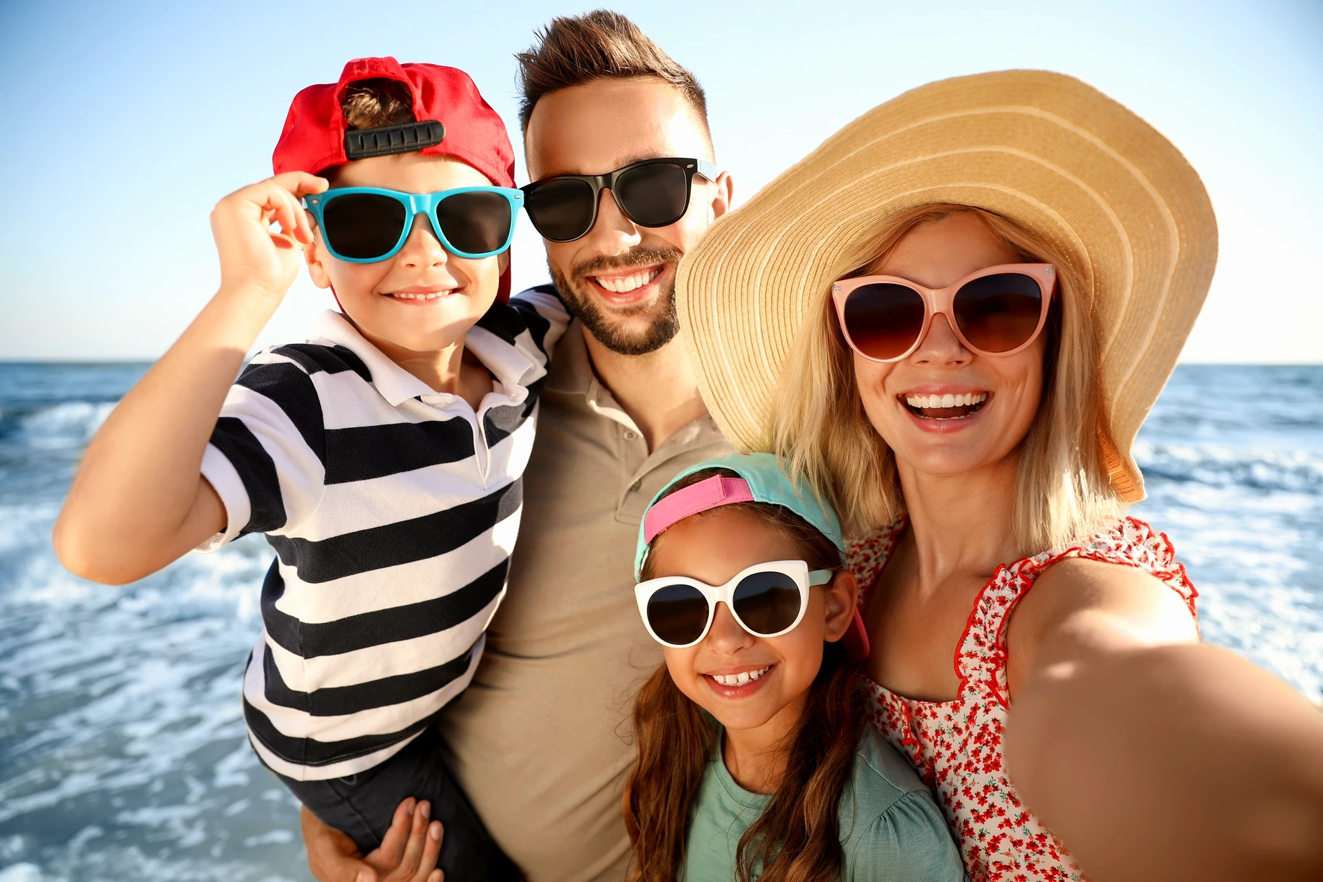 Glückliche Familie mit Sonnenbrillen genießt den Sommer am Strand – optimaler UV-Schutz für Erwachsene &amp; Kinder